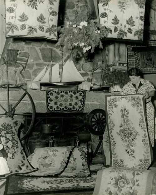 Three dollars a square foot is the average price of these hooked rugs, proudly displayed by an Acadian woman. The price is no measure of the long tiresome homework involved in their manufacture. “Hooked” rugs, an old Nova Scotian handicraft, are made with a hooklike crocheting needle