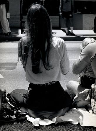 Women seated on curb (seen from behind)